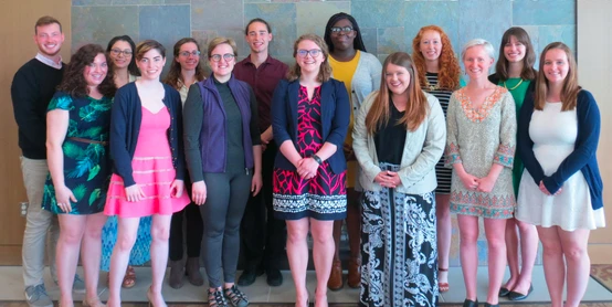 A group of fifteen people from the CAPS Fellows Program pose together, smiling, in front of a tiled wall.