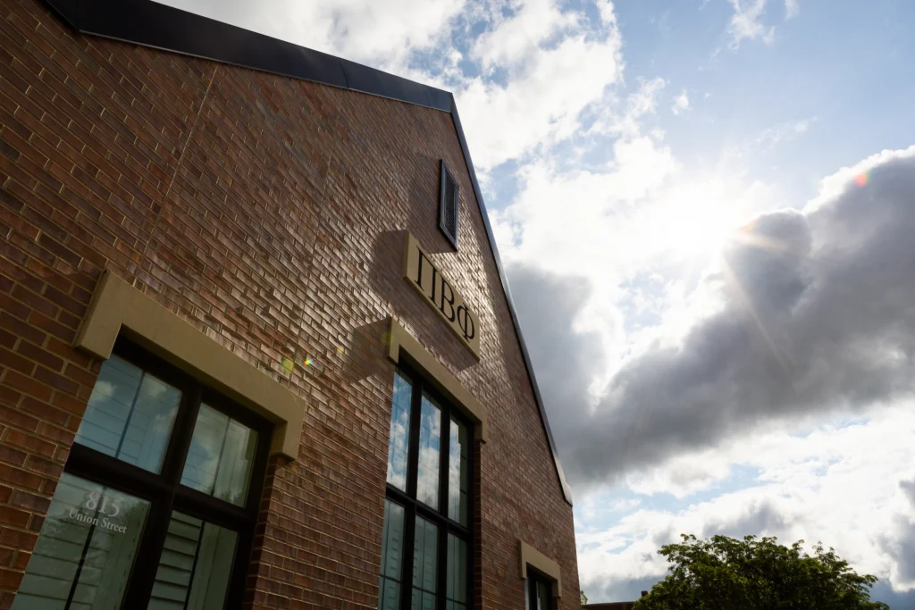 Brick building with large windows and "IBG" sign, sunlight shining through clouds in the sky above, highlights Valparaiso University’s vibrant Fraternity and Sorority Life recognized for its many awards.