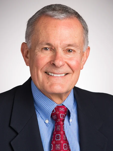 Smiling older man in a suit jacket, blue shirt, and patterned red tie, against a plain background—ready to lead impactful workshops.