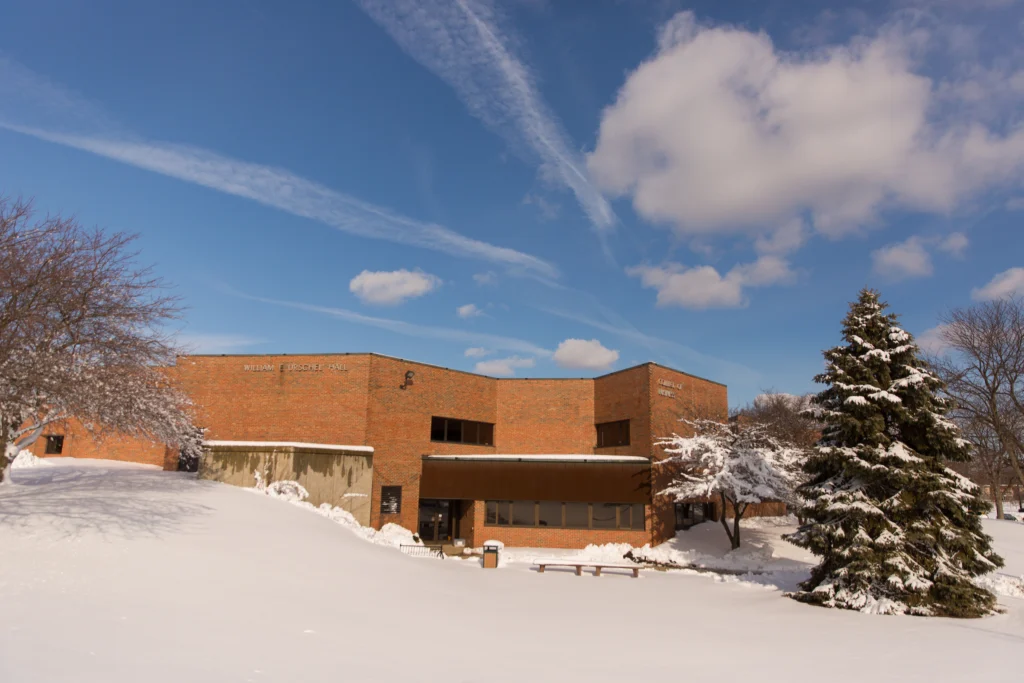 A brick building at Valparaiso University sits amid snow-covered ground and trees under a blue sky with clouds.