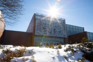 A modern building with a decorative facade, sunlight shining above, and snow covering the ground and bushes—an inspiring setting for Symphonia’s commitment to music education.