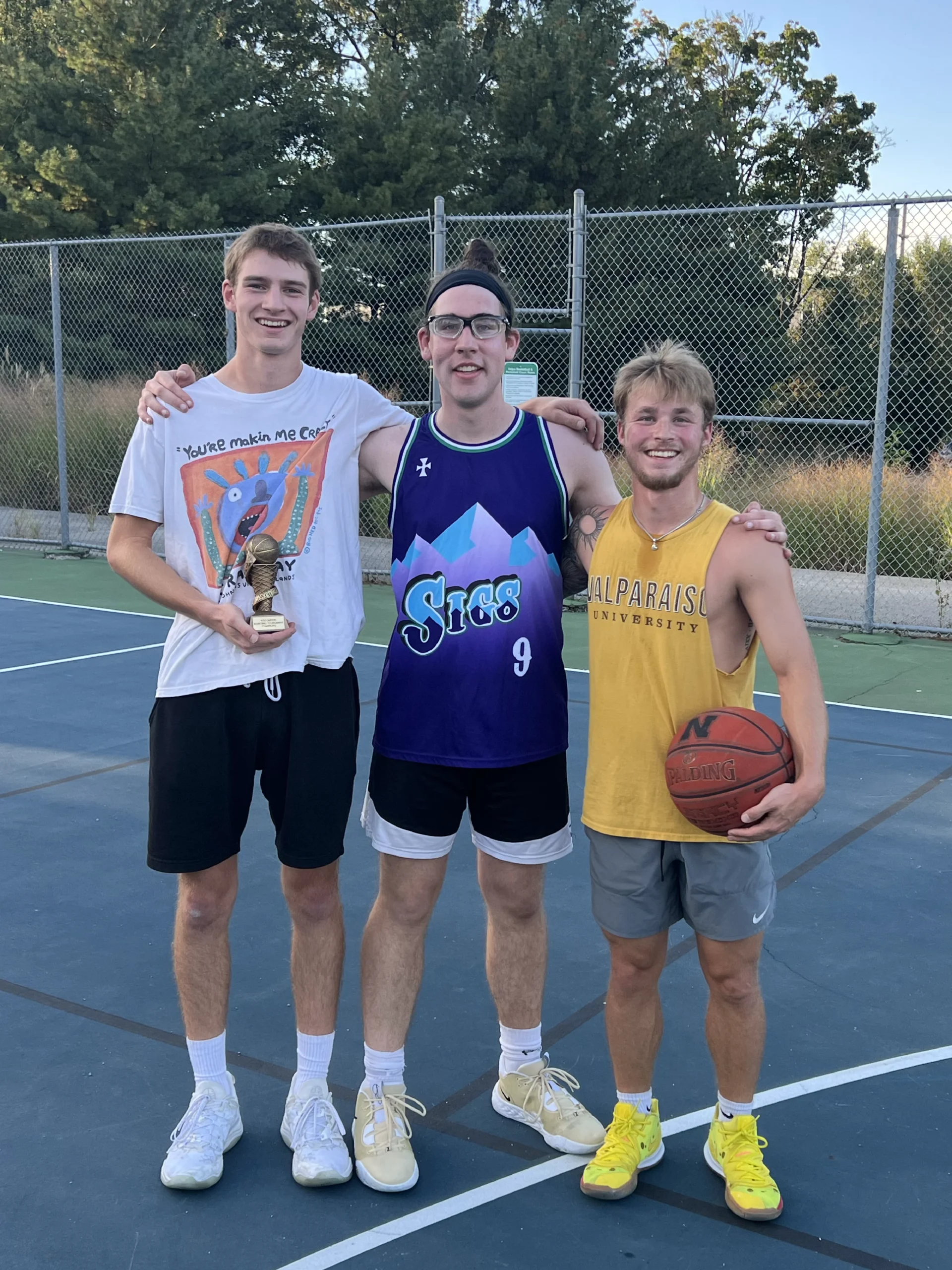 Three young men smiling on an outdoor basketball court, one holding a ball, posing for a photo together—capturing the spirit of friendship in this Beacon's Reflection moment.