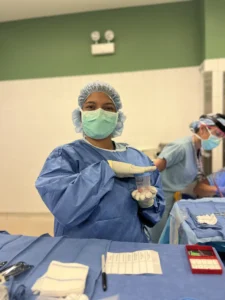 A surgeon in scrubs holding a specimen cup in an operating room, with another medical worker in the background—an OMP Spotlight moment capturing dedication and precision.