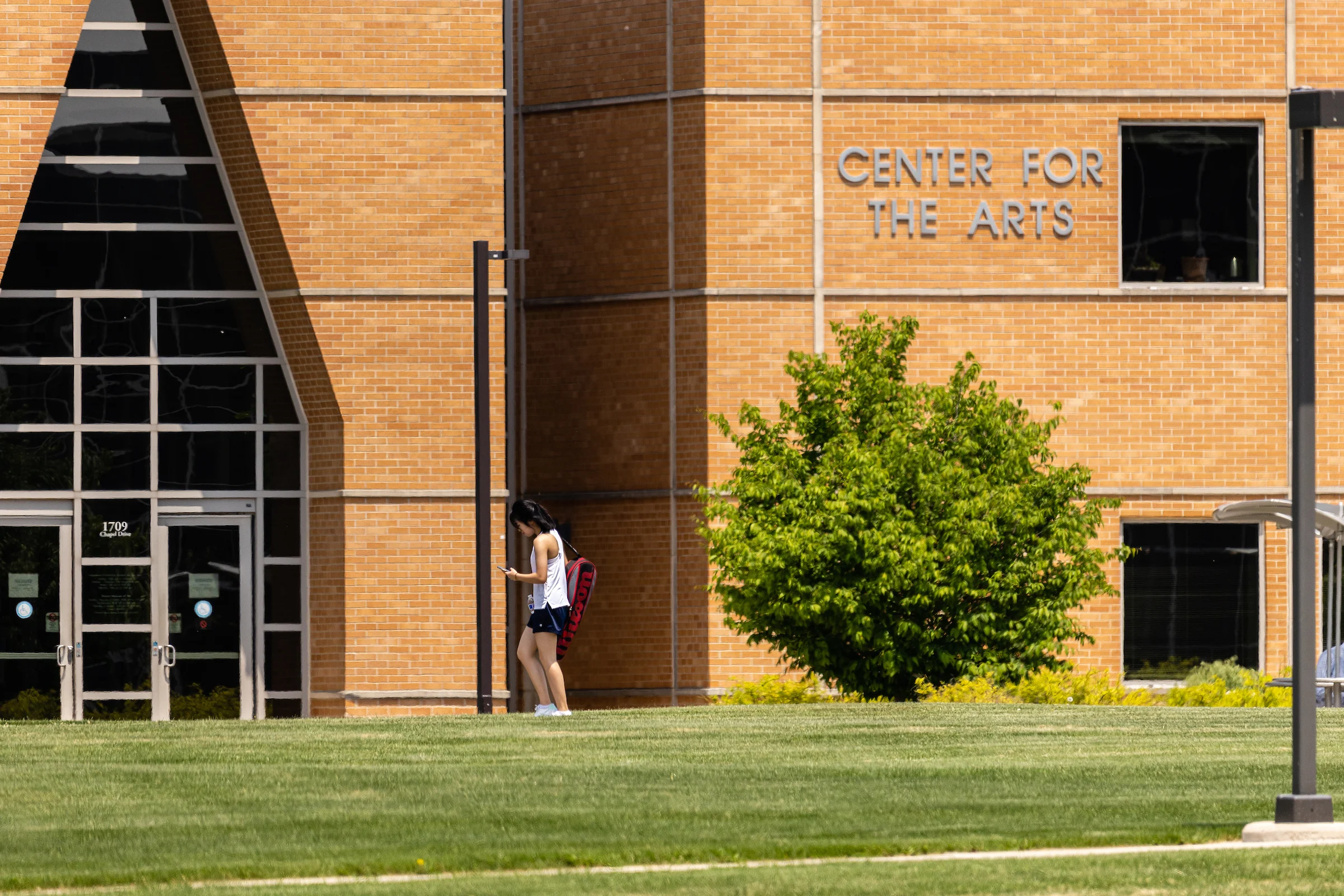 A student walks outside the Center for the Arts building on a sunny day, where vibrant exhibitions and series often inspire creativity.