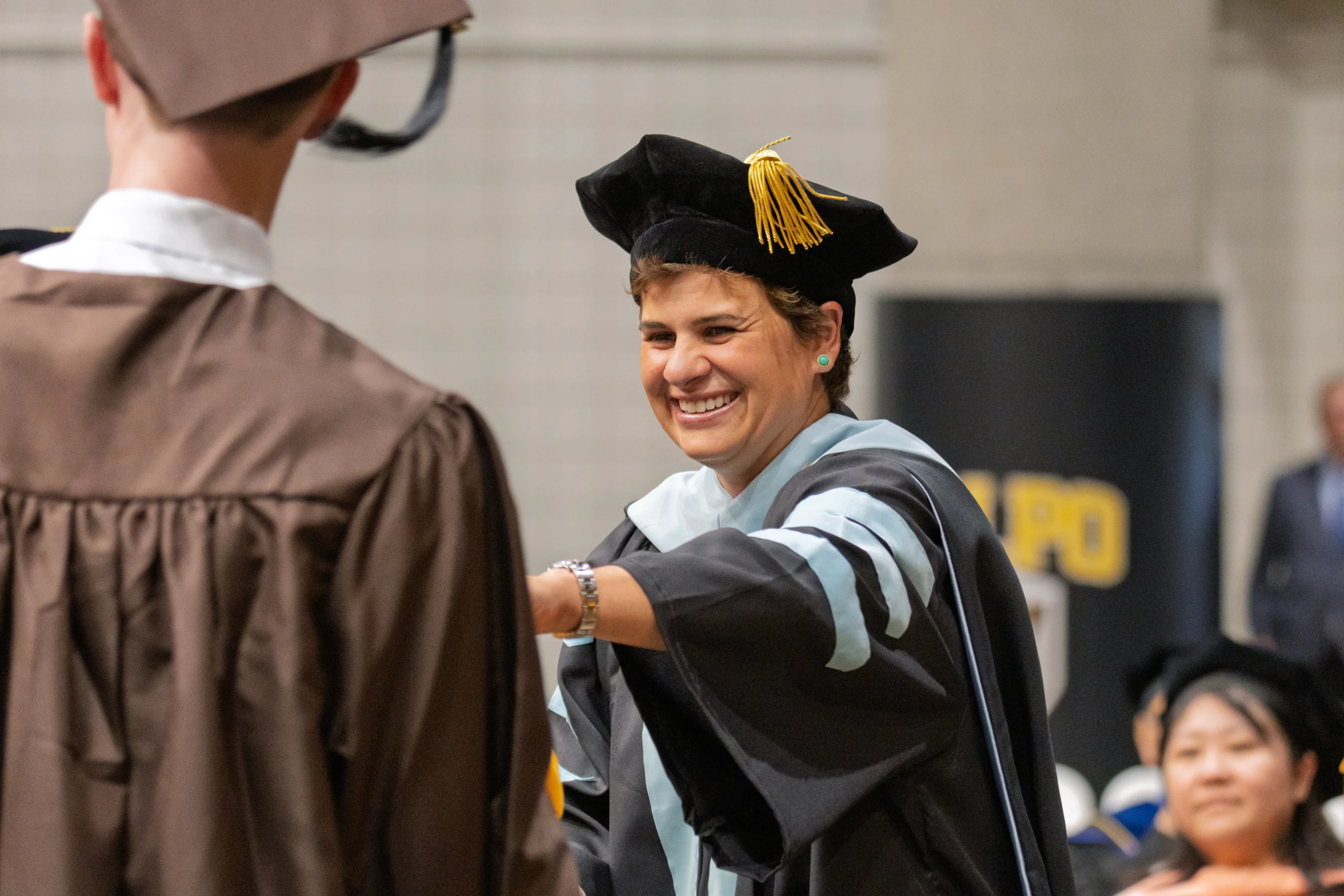 A smiling faculty member in academic regalia congratulates a graduate during the Commencement ceremony.