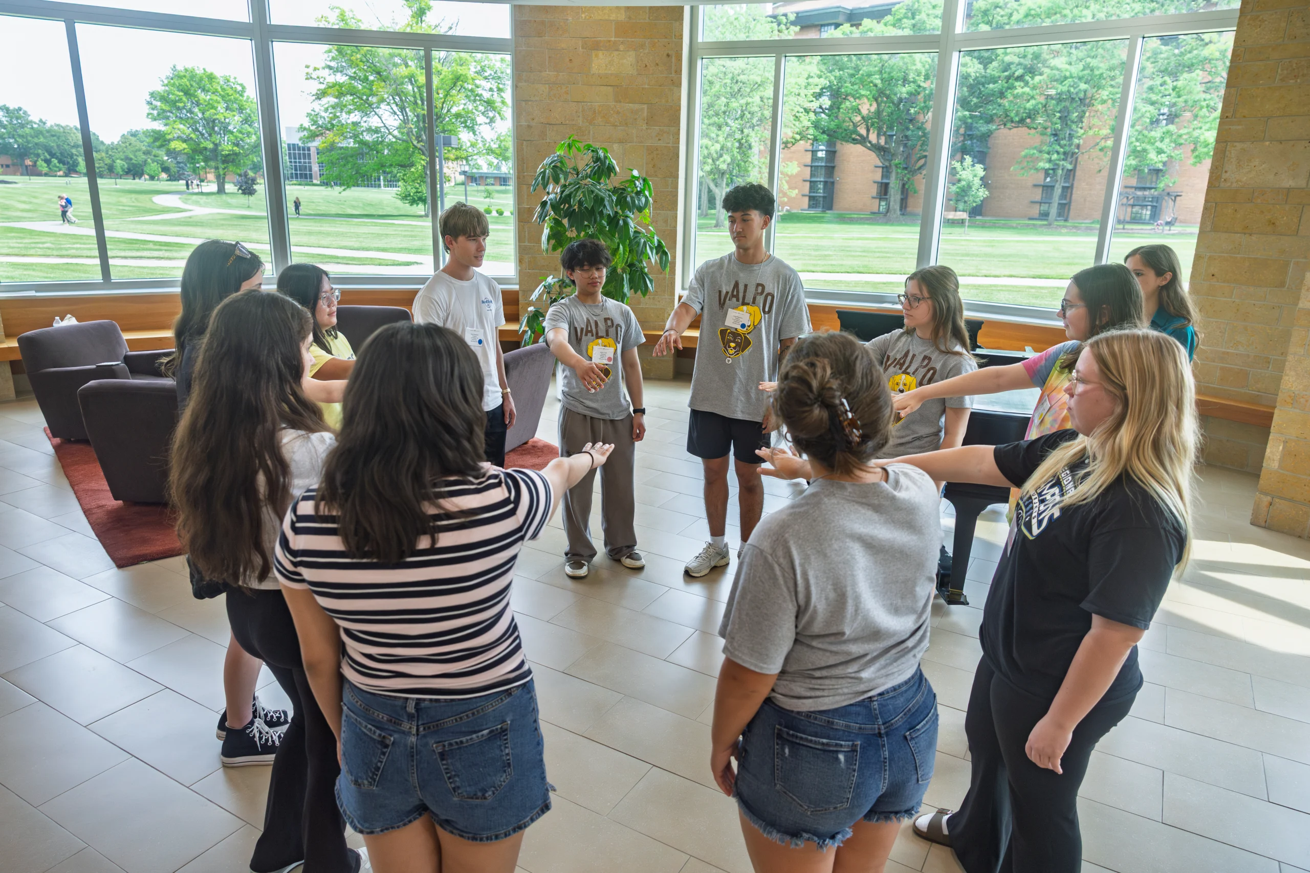 A group of students stands in a circle indoors, reaching their hands toward the center with FOCUS for an activity.