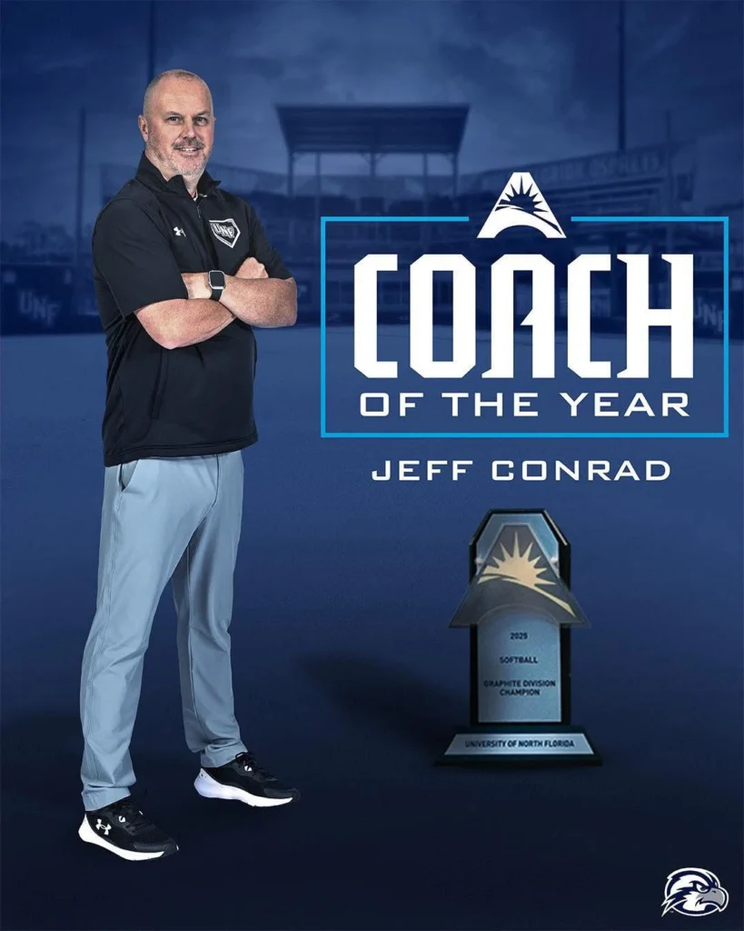 A man in athletic wear stands by a trophy and a "Coach of the Year" sign, proudly featuring Beacon coach Jeff Conrad's name below.