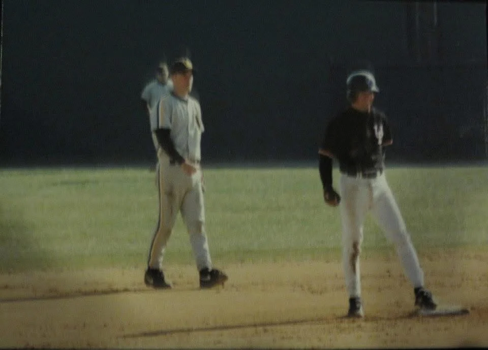 Two baseball players stand on a sunlit field, with Jeff Conrad ready as a beacon of focus—one positioned on base and the other in the infield.