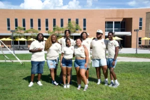 A group of eight people in matching beige shirts and denim shorts stand smiling on grass in front of a brick building, celebrating Valpo BSO and Black History Month.