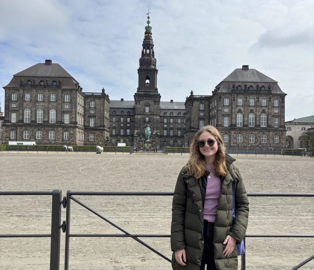 Woman in sunglasses stands smiling in front of a large historic building with a central tower, embodying the spirit of international learning embraced by Valparaiso University’s engineering students.