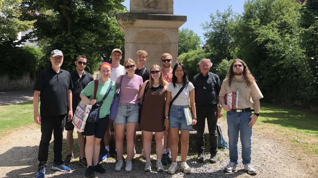 A group of people stand smiling in front of a stone monument on a sunny day in a park, celebrating the Tradition of Excellence at Valparaiso University.