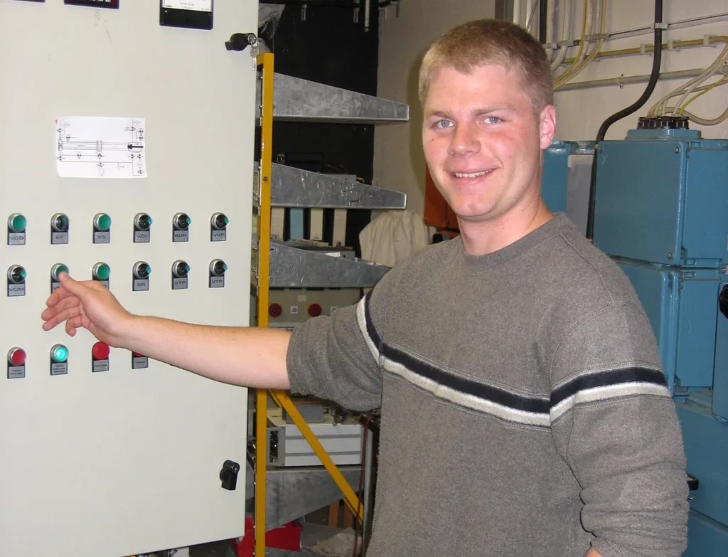 A smiling man presses a button on an industrial control panel in a technical room, showcasing hands-on experience valued by engineering students at Valparaiso University.