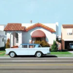 A vintage light blue car is parked on the street in front of a white house with a red tiled roof.