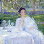 Woman in a white dress sits at a table outdoors, surrounded by tea items, under dappled sunlight.