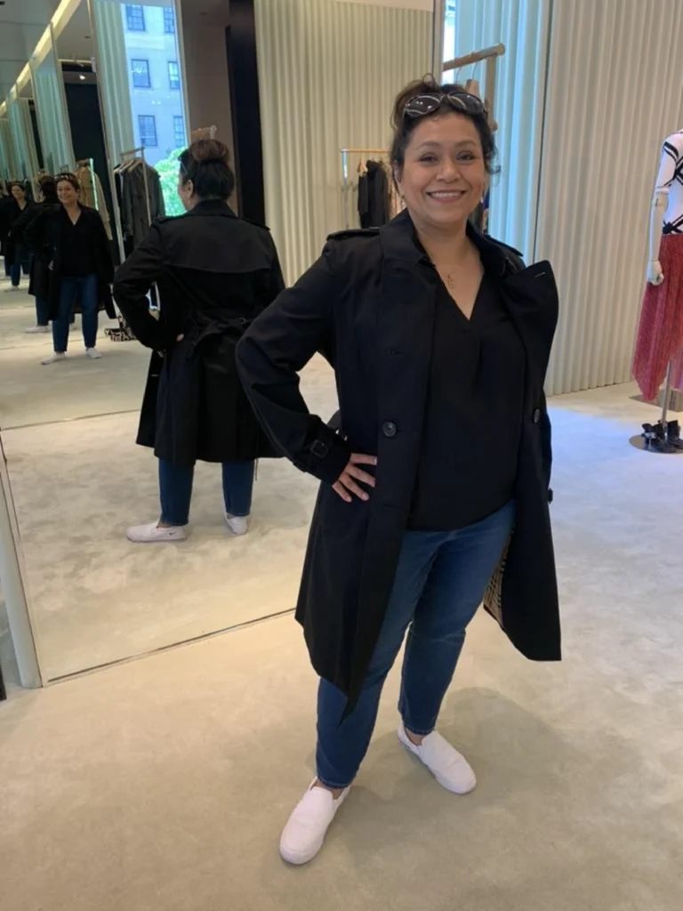 Izzy Ibarra beams in a black coat and white shoes, posing confidently in front of a mirror at Beacon's Reflection clothing store.