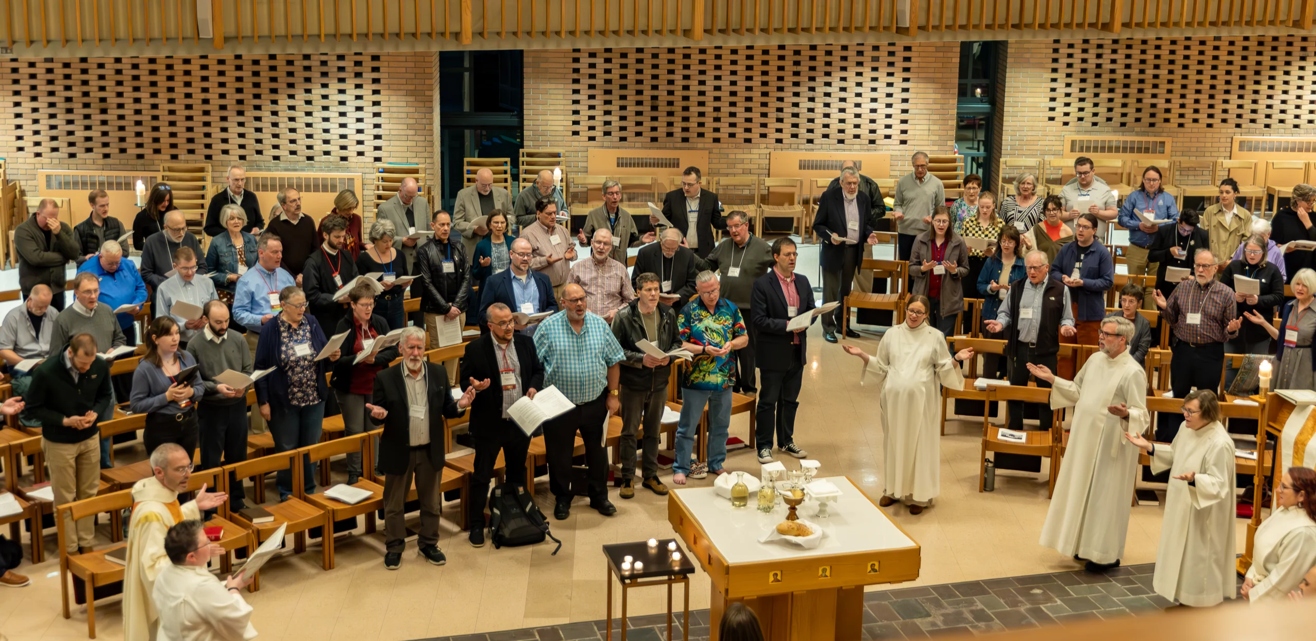 A large group of people sing and worship in a church, with clergy in white robes leading at the front during a special service about the conference.