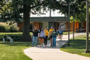 A group of students preparing for college walk together on a sunny sidewalk in front of a campus building.