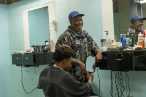 A barber smiles while chatting with a customer in a brightly lit barbershop, exemplifying an OMP Spotlight moment of genuine connection and service.