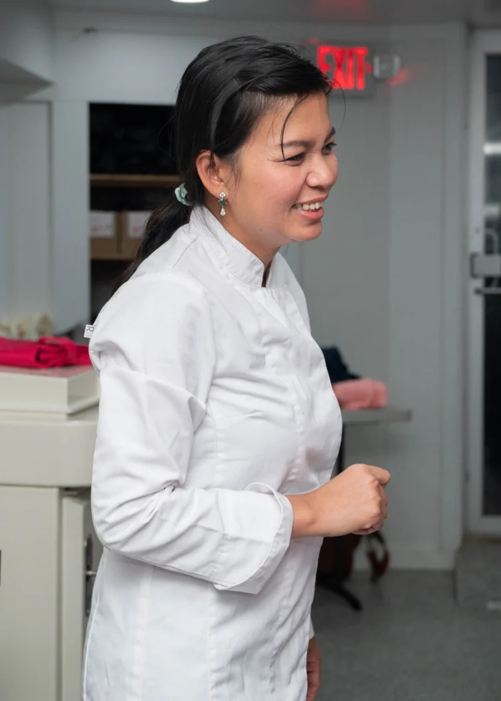 A woman in a white chef's coat smiles while standing indoors near an exit sign, embodying Valpo’s commitment to experiential learning through the French program.