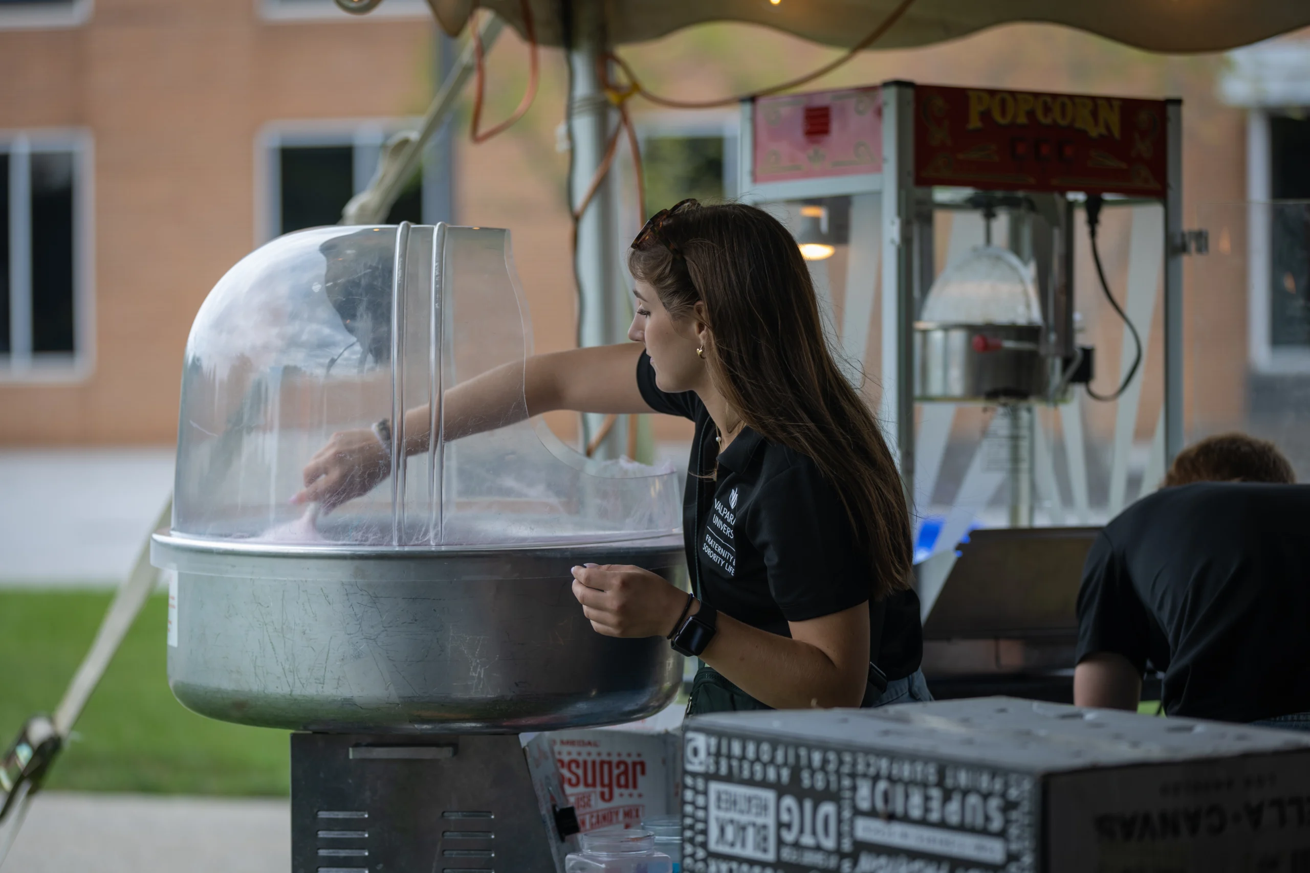A woman operates a cotton candy machine at an outdoor event hosted by the University Programming Council, with a popcorn machine in the background.