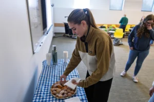 A woman places pastries on a napkin from a plate on a table covered with a blue checkered cloth, recreating the ambiance of Valpo’s French program and its focus on experiential learning.