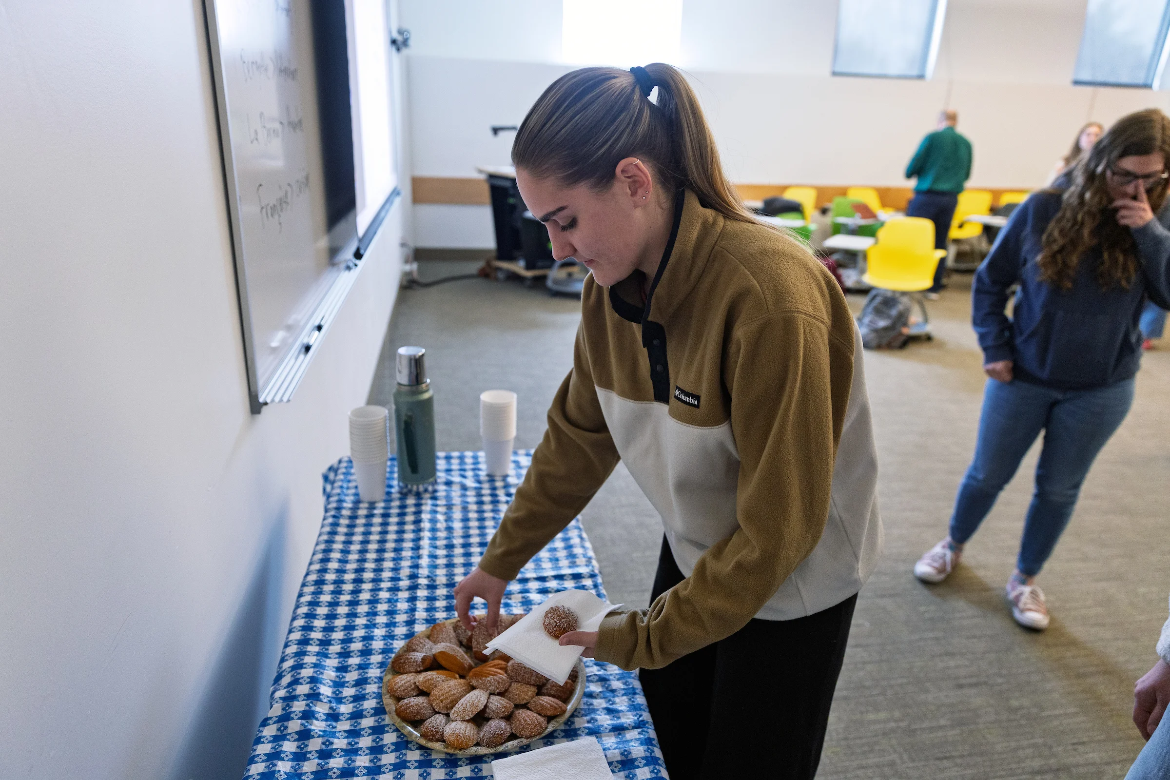 A woman places pastries on a napkin from a plate on a table covered with a blue checkered cloth, recreating the ambiance of Valpo’s French program and its focus on experiential learning.