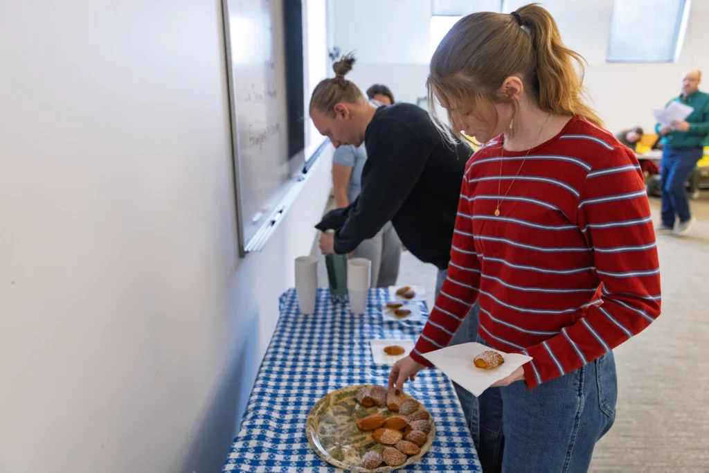 Two people take cookies from a platter on a blue checkered tablecloth at an indoor Valpo event, highlighting the French program’s focus on experiential learning.