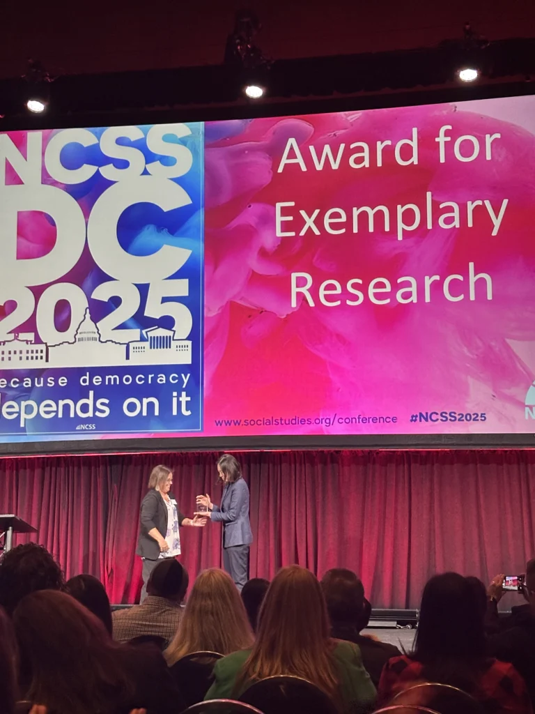 Two people on stage at a national conference, presenting the "Award for Exemplary Research" at NCSS DC 2025—highlighting Valpo Education's commitment to excellence in research.