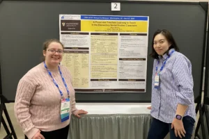 A Valparaiso University education professor and student stand in front of a research poster about elementary social studies teaching at a national conference.
