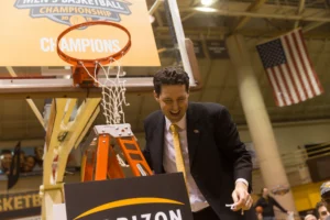Bryce Drew, 2026 Commencement Speaker at Valpo, smiles in a suit while cutting a basketball net after winning a championship game.