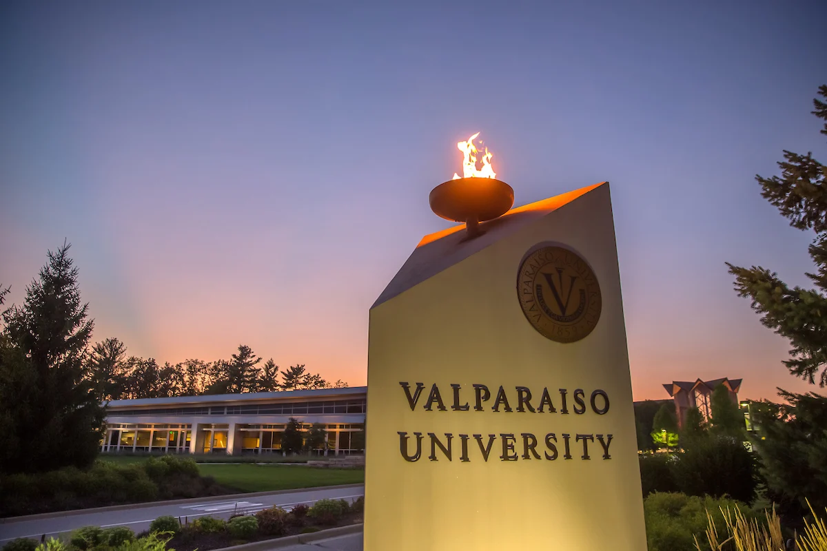 A Valparaiso University sign with a lit torch at sunset, campus buildings in the background—an inspiring setting for pursuing a Master’s Program in Organizational Leadership.
