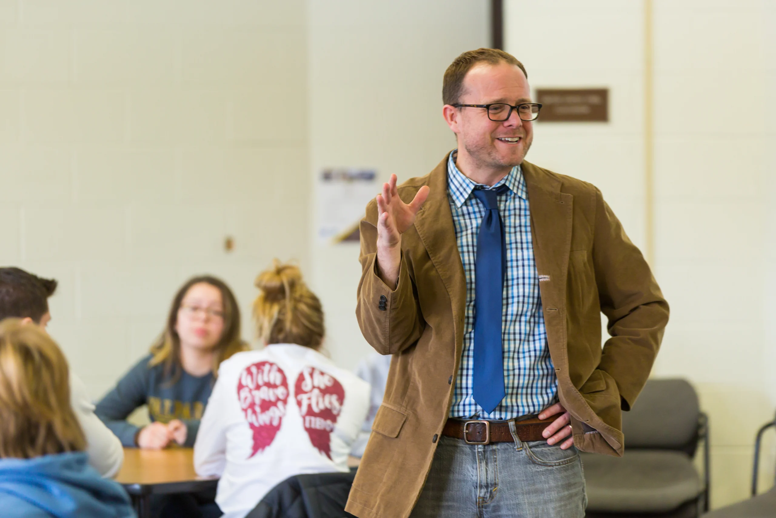 A man in glasses and a brown jacket speaks to seated students in a classroom, discussing concepts from the Integrated Business and Engineering program.