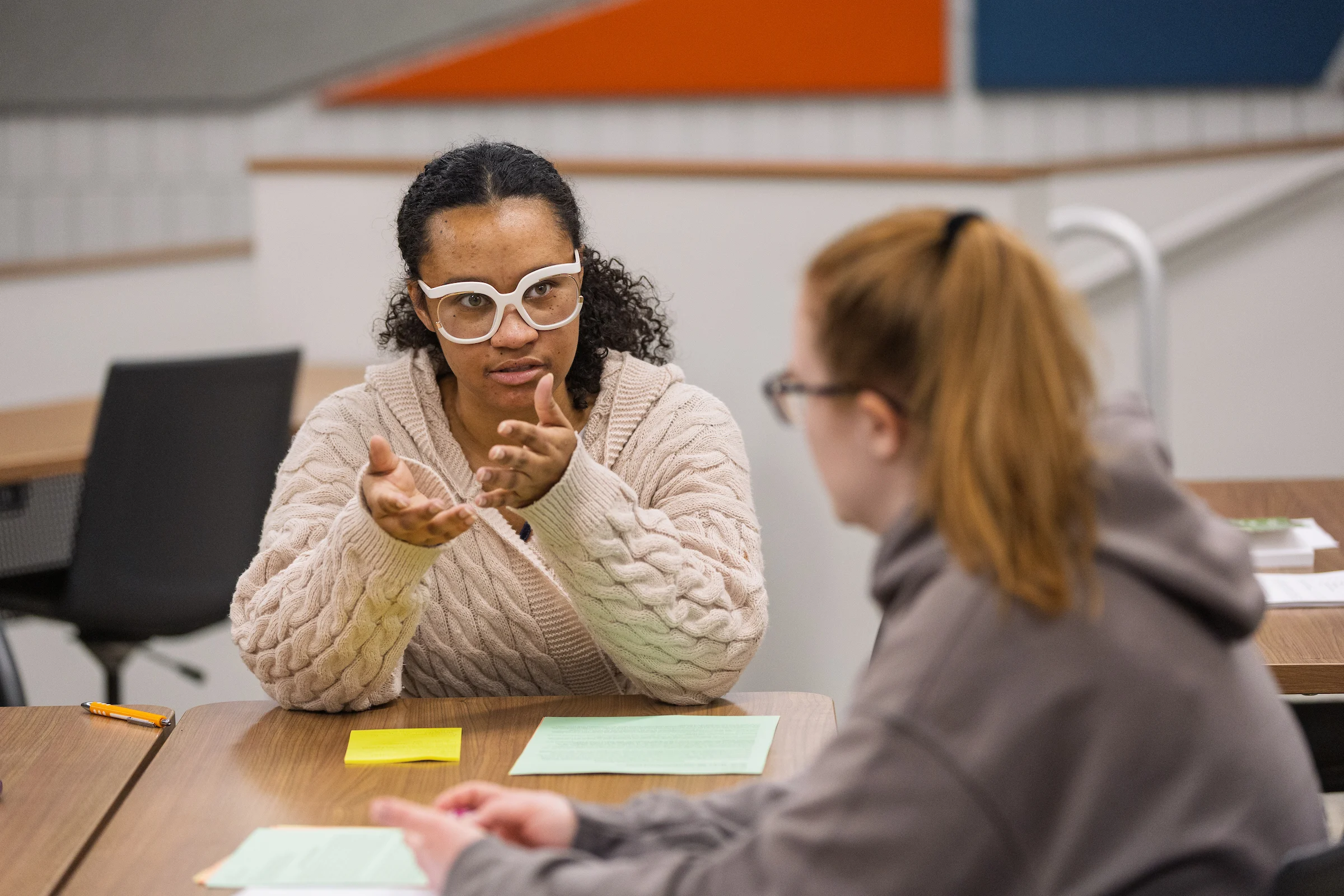 Two people sit at a table talking, with papers and a pencil in front of them in a classroom setting at Valparaiso University, discussing topics in public safety social work.