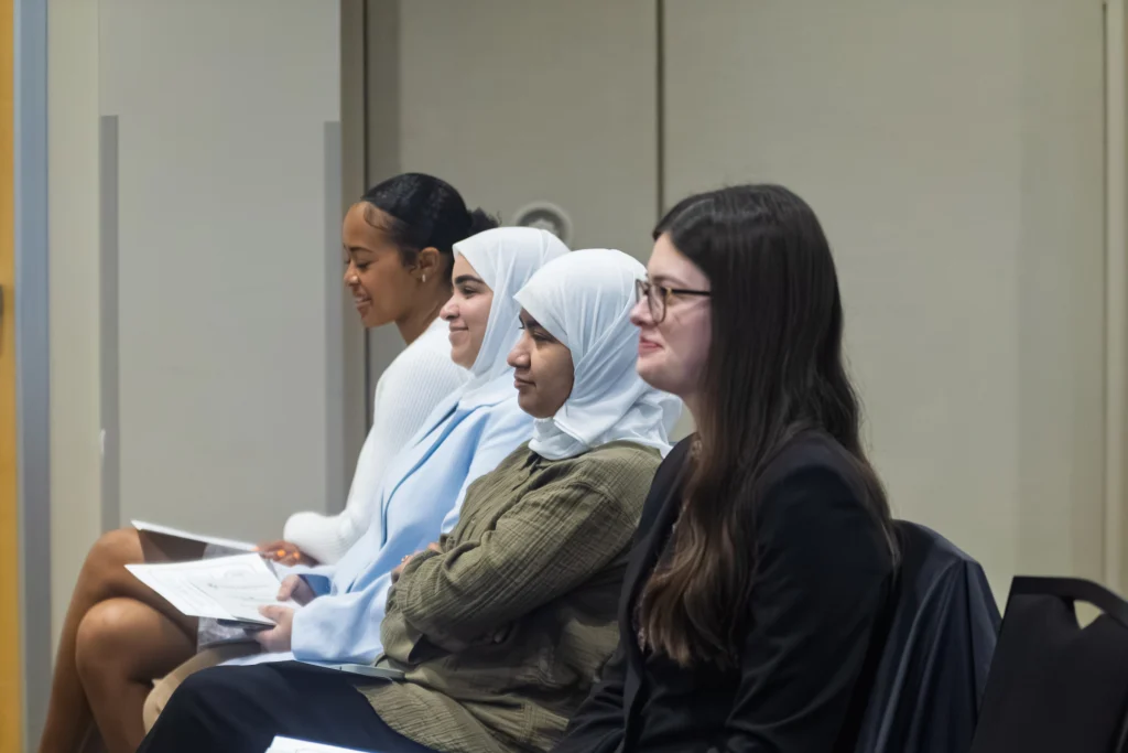 Four women sit in a row, holding papers and attentively listening at a Valparaiso University Human Science Honor Society, Kappa Omicron Nu, event.