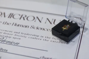 A certificate and a small open box with a Kappa Omicron Nu Human Science Honor Society pin inside are shown close up.