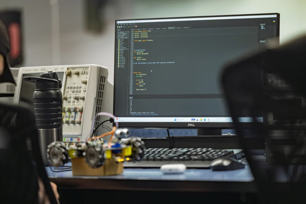 A computer monitor displays code next to electronics equipment and a small robotic vehicle on a desk, reflecting the hands-on Computer Engineering projects at Valpo that foster a collaborative community.