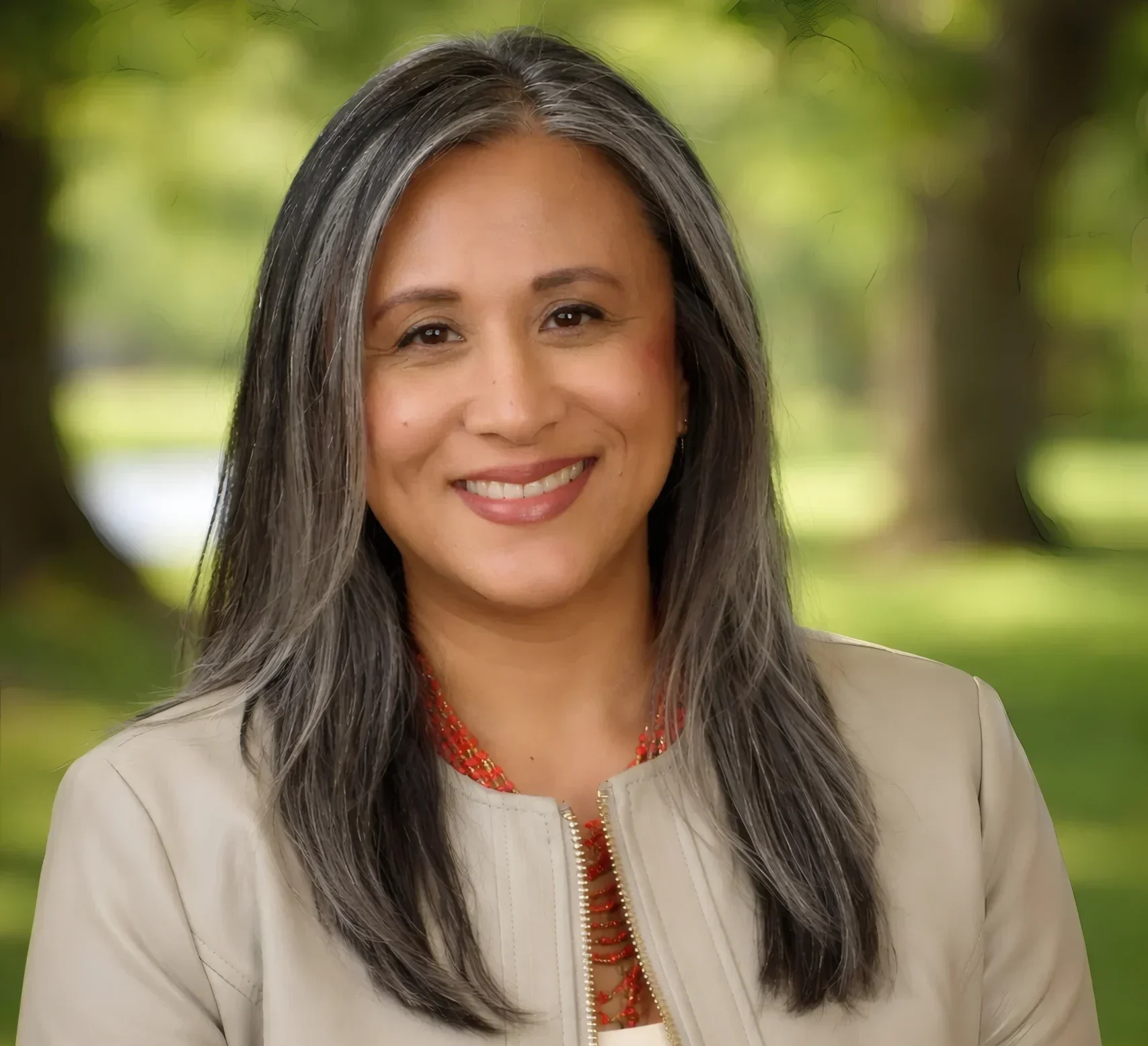 Smiling woman with long gray hair stands outdoors, wearing a beige jacket and red necklace—Dr. Mary Grace Almandrez, Senior Vice President at Valparaiso University.