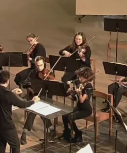 Four violinists, led by a conductor, perform on stage with music stands, bringing Beacon's Reflection to life in a captivating musical display.
