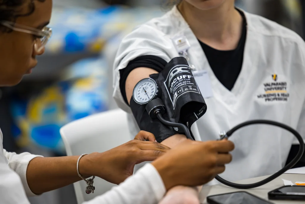 A healthcare student, pursuing one of many interesting majors, measures another person's blood pressure with a cuff and gauge.