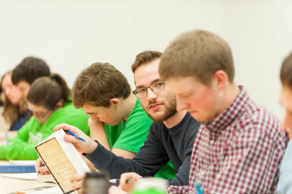 Students sitting at a table, reading and discussing a book in a classroom setting, explore interesting majors that can lead to surprising careers.