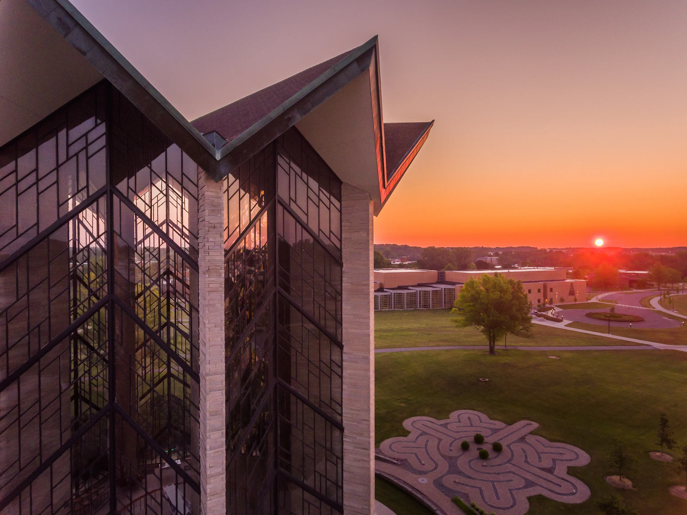 A modern building with large glass windows at sunset, home to the Institute for Leadership and Service, overlooking a green lawn and garden maze.