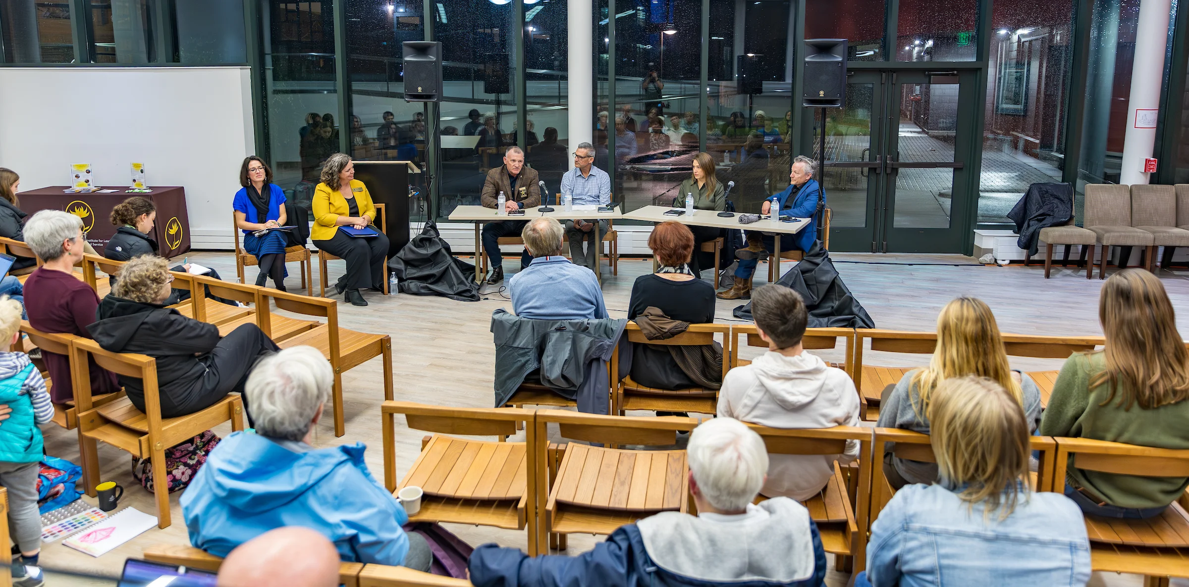 A panel of five people from the Institute for Leadership and Service speaks to an audience seated on wooden chairs in a bright, modern room.