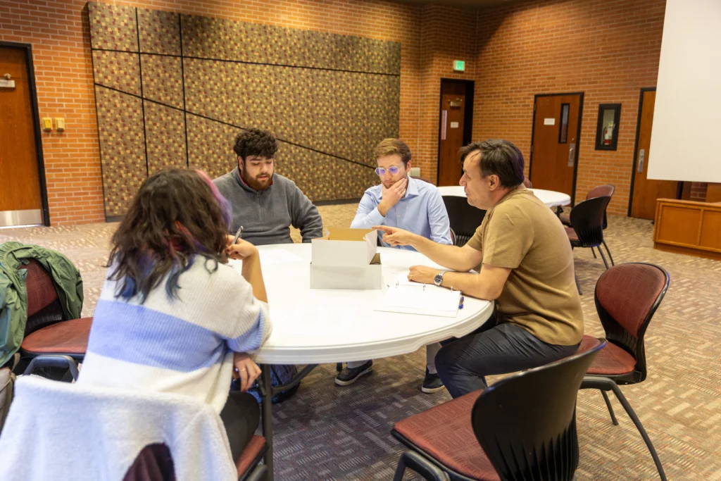 Three students and a professor sit around a round table in discussion, with a laptop and papers in a conference room, discussing the latest issue of Letras, the Spanish Literary Magazine at Valpo.