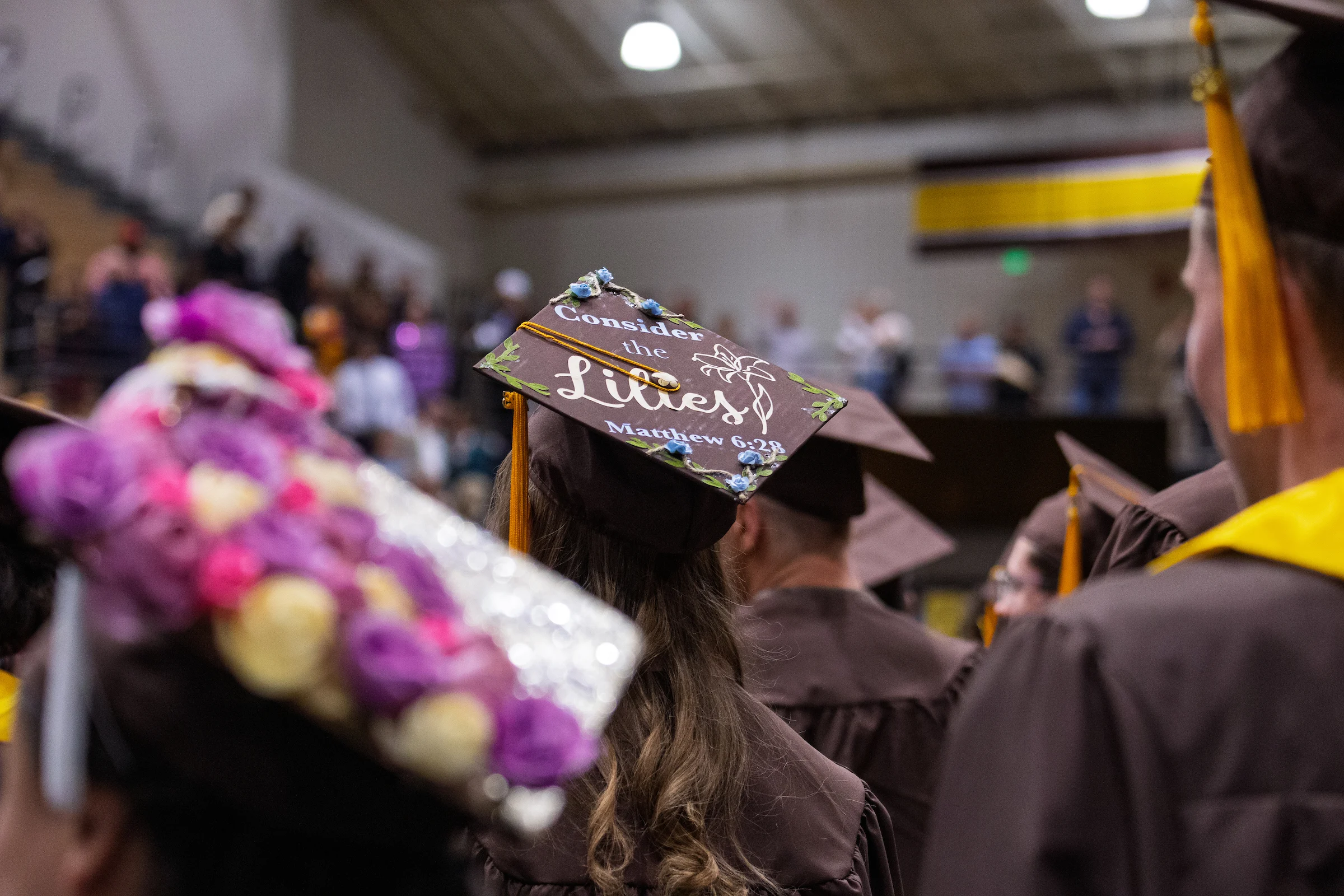 Graduate in cap and gown with a decorated cap reading "Consider the Lilies, Matthew 6:28," at Valparaiso University's ceremony for Occupational Therapy Doctorate program graduates.