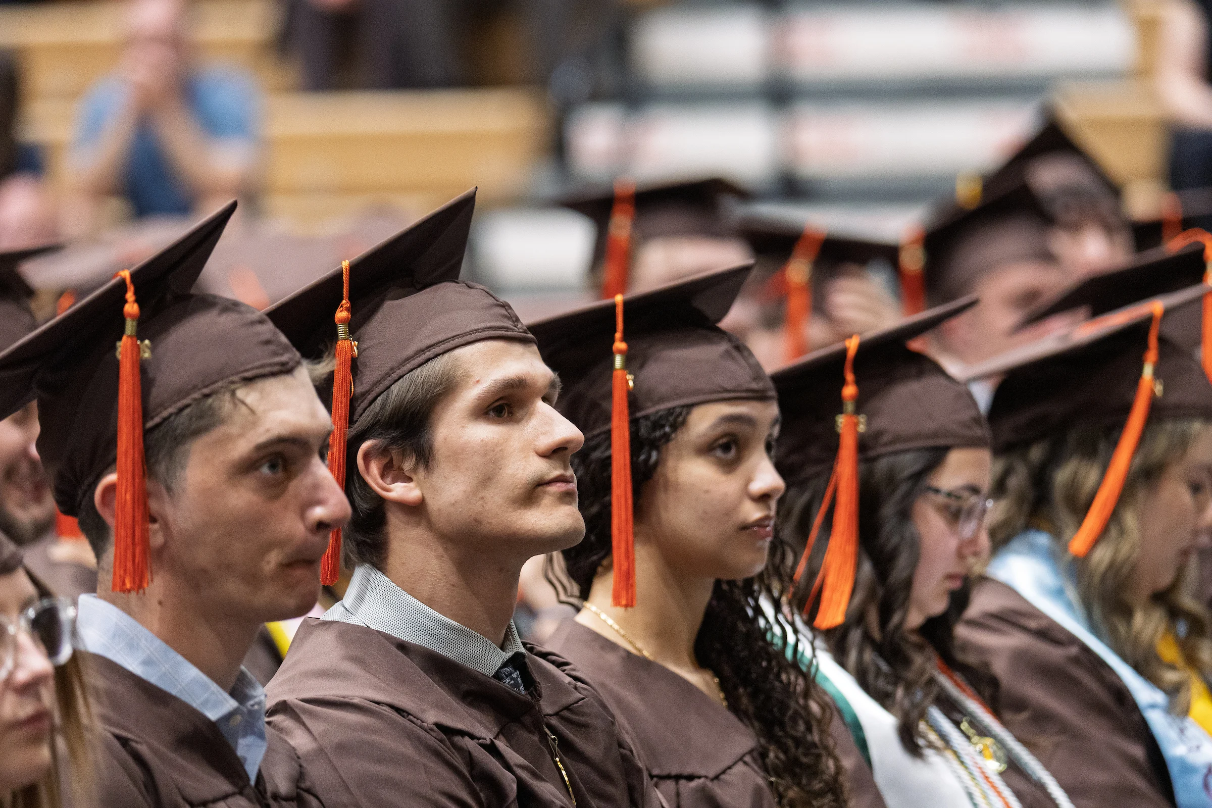 Graduates wearing brown caps and gowns sit in rows, attentively watching the Valparaiso University graduation ceremony, ready to enter the job market.