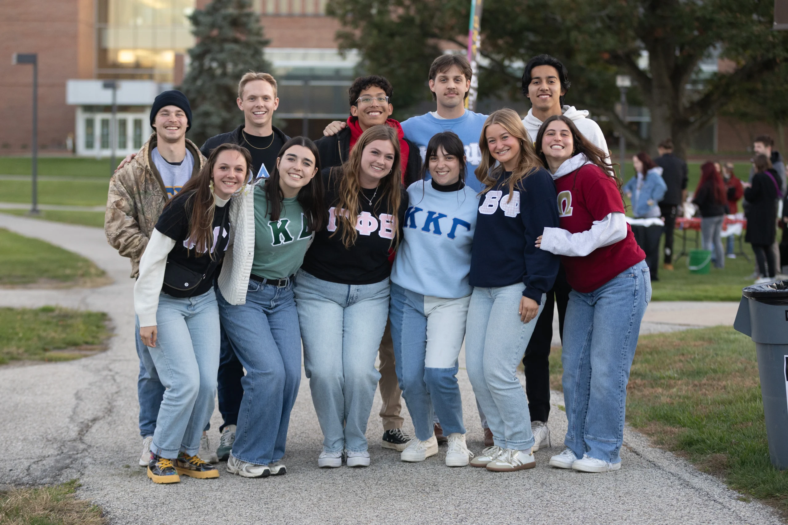 A group of smiling college students in Greek letter shirts pose together outdoors on campus, showcasing their strong sense of Student Involvement.