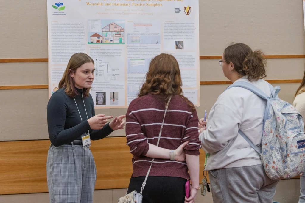 A woman presents a student research poster to two other women at an academic event, showcasing discoveries from Valparaiso University in preparation for SORCE 2026.