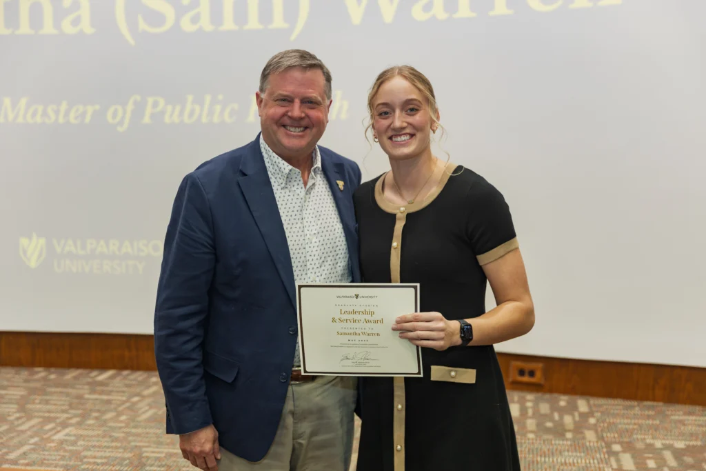 Two people smiling; one holds an Excellence in Leadership & Service Award certificate at a Valpo event, celebrating an Honors Graduate Student's achievement.