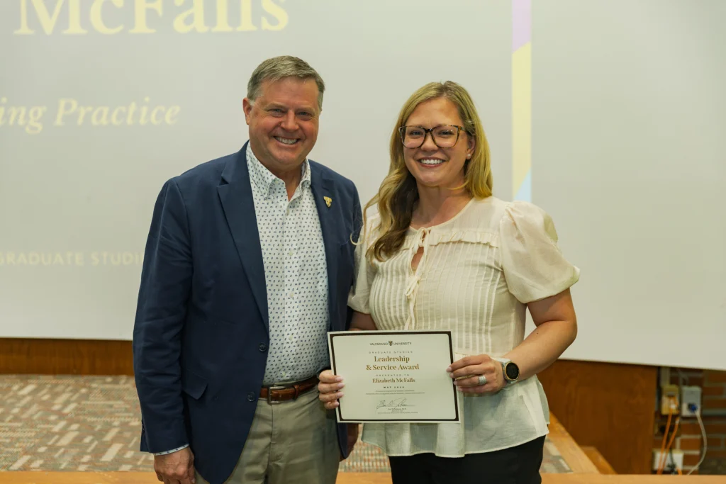 Two people smiling in an indoor setting, one holding a "Leadership & Service Award" certificate, celebrating Student Excellence at Valpo.