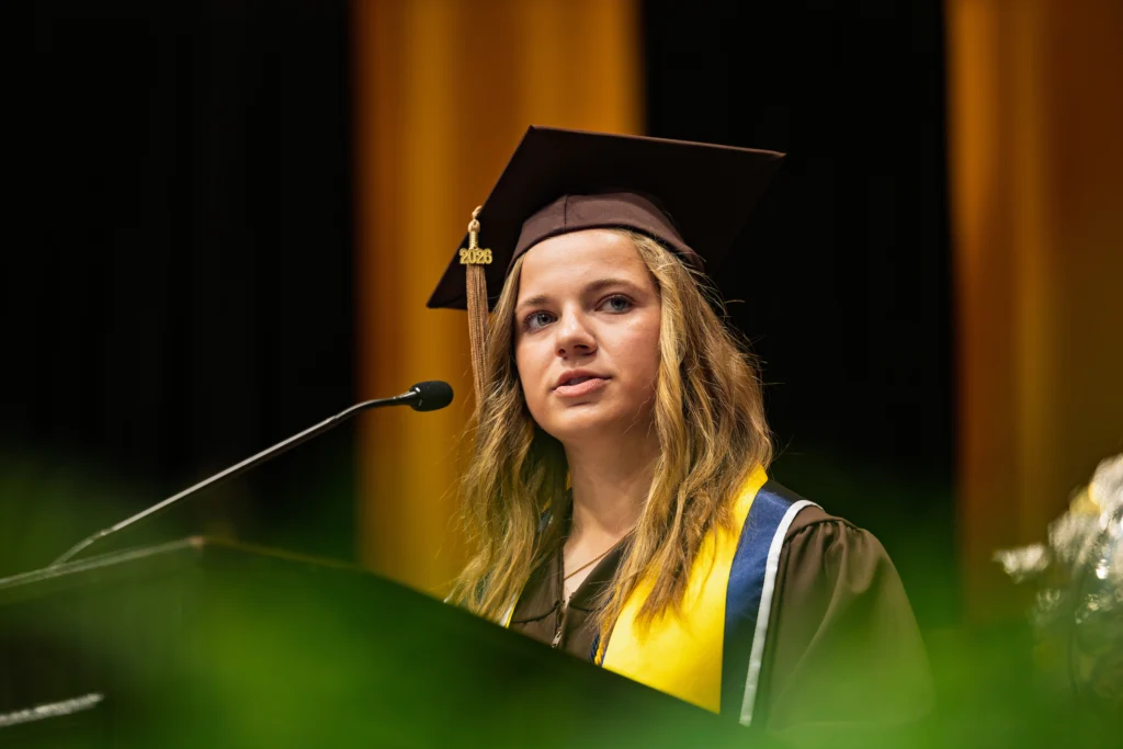 Young woman in graduation cap and gown speaks at a podium during the Valparaiso University Graduation Ceremony for the Graduating Class of 2026.